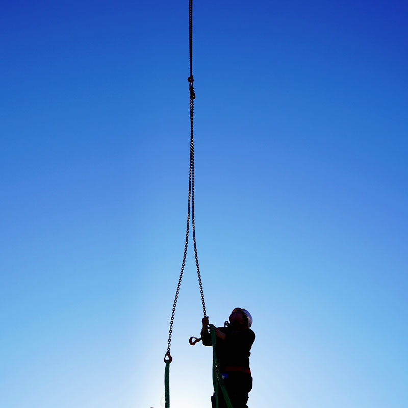 Die Silhouette eines Bauarbeiters mit Helm vor der Sonne der Ketten an ein Bauelement montiert